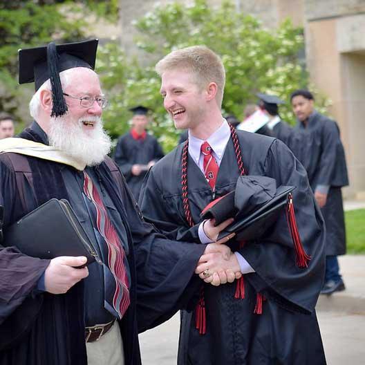 A graduate laughs with a professor as they prepare for Commencement